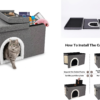 A close-up of an open grey pet house revealing a pink strawberry-print cushion and various cat supplies. A grey cat walks through the plush-lined front portal, with the open lid leaning against the side.