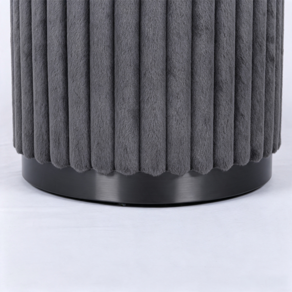 Dark gray pleated velvet storage stool placed next to a cozy bed in a warm bedroom setting.