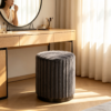 Dark gray pleated velvet round storage ottoman stool styled in front of a wooden vanity desk in a sunlit room.