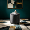 Dark gray fluted velvet round storage ottoman stool in a moody modern room setting.