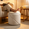 White round textured fabric ottoman used as a comfortable footrest by the sofa