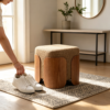 Beige fabric square ottoman stool used as a footrest and seating in a bedroom