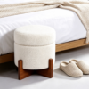 Small white boucle vanity footstool placed at the end of a bed in a cozy contemporary bedroom