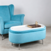 Modern light blue oval velvet storage footstool used as a coffee table next to a navy blue sofa in a minimalist living room.