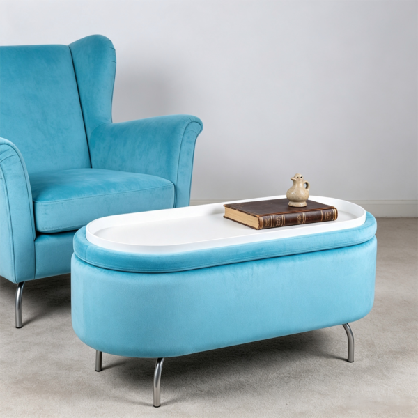 Modern light blue oval velvet storage footstool used as a coffee table next to a navy blue sofa in a minimalist living room.
