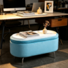 Light blue velvet oval storage ottoman with gold trim set in an elegant room with dark wood furniture and classic decor.