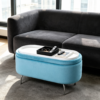 Light blue velvet oval storage ottoman featuring thin metal legs and a reversible wooden top tray in a modern living room setting.