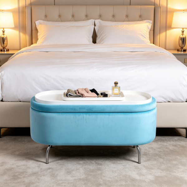 Light blue velvet oval ottoman storage bench placed near a bed with warm beige bedding and cozy neutral decor.