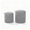 Two grey round upholstered storage ottomans with fabric covers and side leather handles