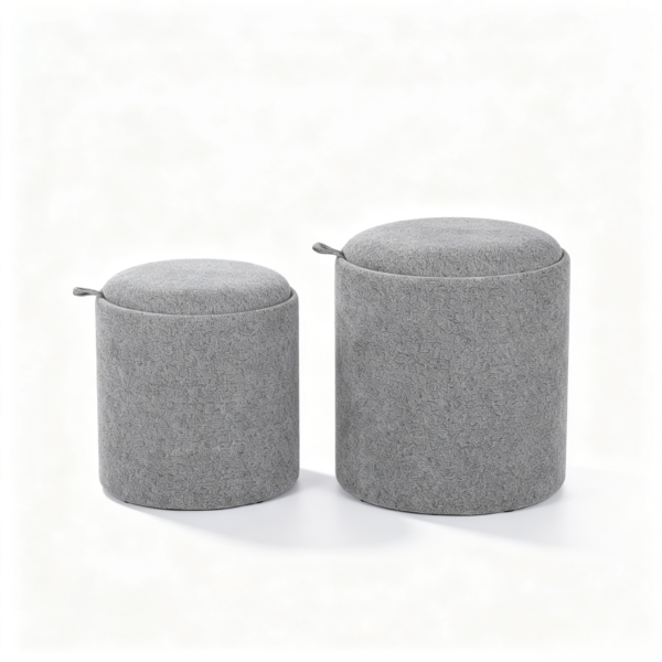 Two grey round upholstered storage ottomans with fabric covers and side leather handles