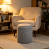 Grey round upholstered ottoman footstool placed in front of an armchair in a cozy living room