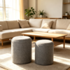 Compact grey fabric cylindrical ottoman used as a footrest and side seat next to furniture